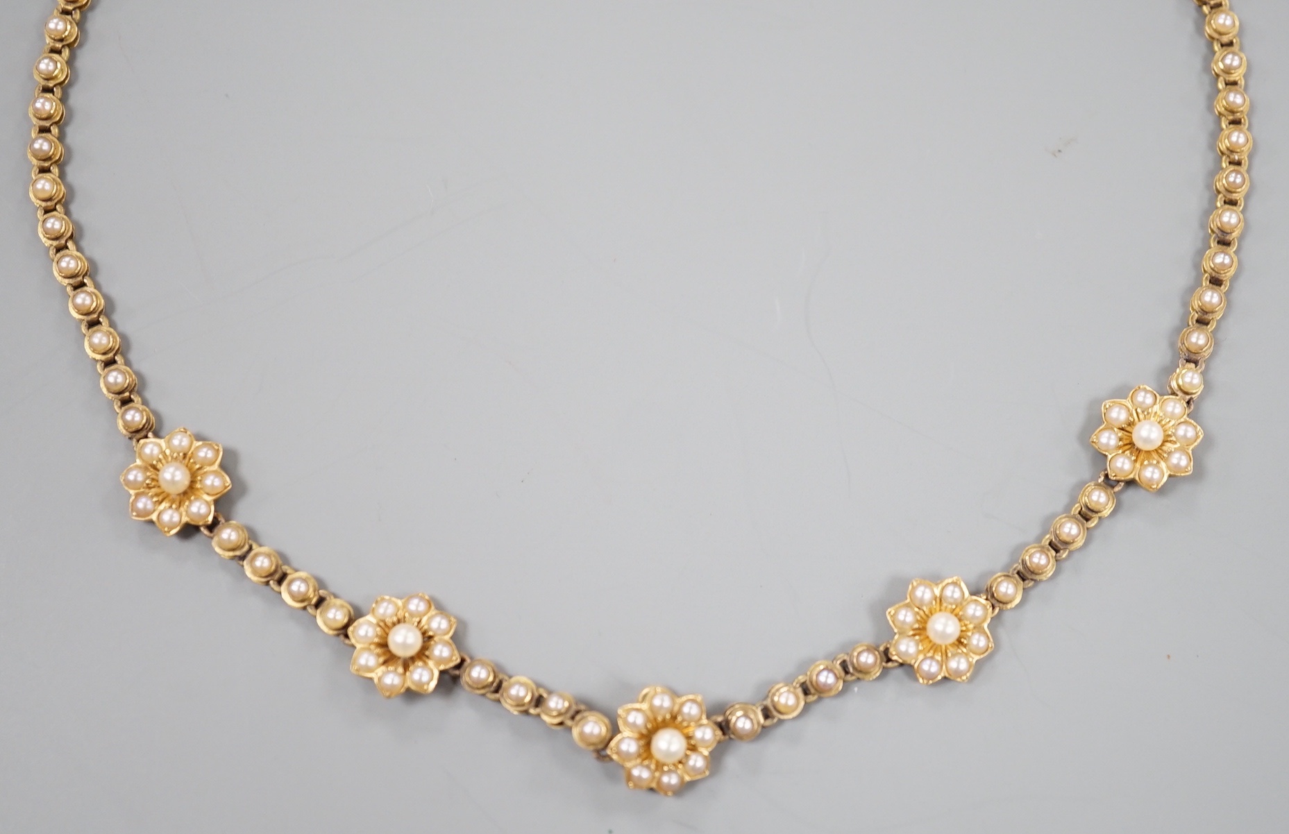 A late Victorian yellow metal and seed pearl set flower head motif necklace, (lacking drop pendant), 36cm, gross weight 18 grams.